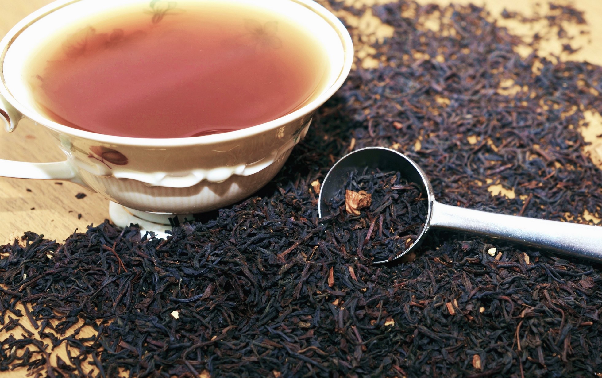ceai negru uscat varsat pe masa langa o ceasca cu ceai infuzat